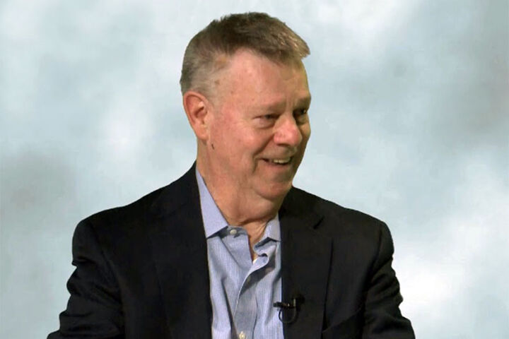 Tim Seiler speaks in front of a white and grey backdrop.